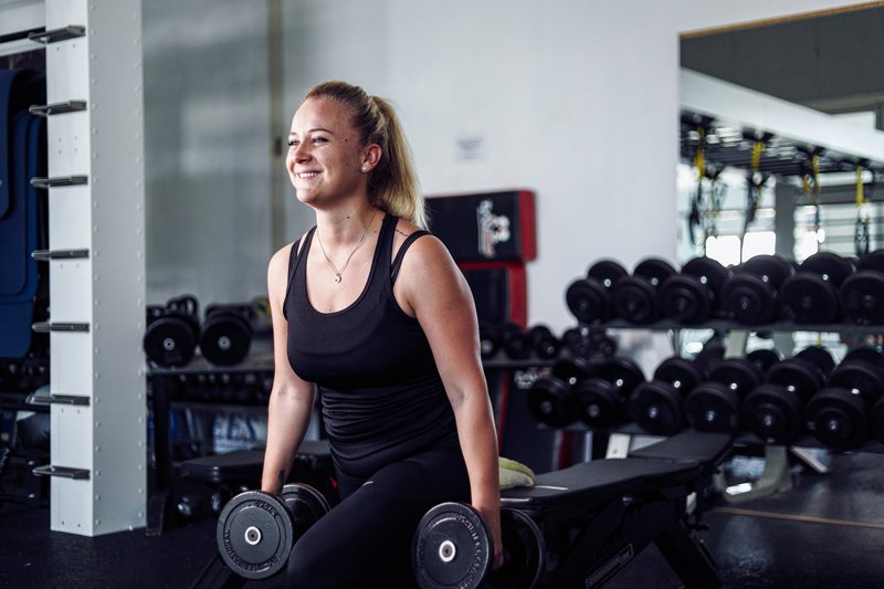 Frau übt Krafttraining mit Kurzhanteln und laechelt