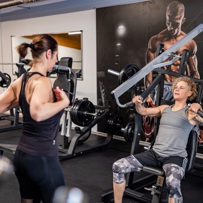 Trainerin betreut Kundin beim Krafttraining an einer Brustpresse