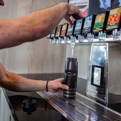 Person lässt sich ein Getränk aus der Fruttibar raus