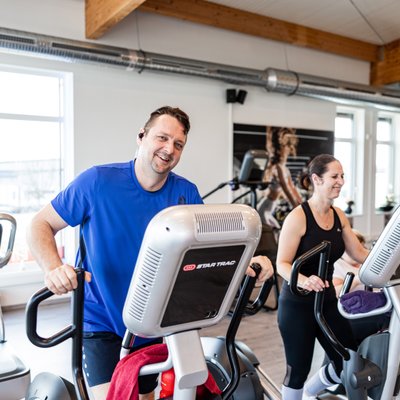 Zwei Personen trainieren lachend auf Crosstrainern